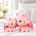 Pink winged cat plushie on a cozy bed